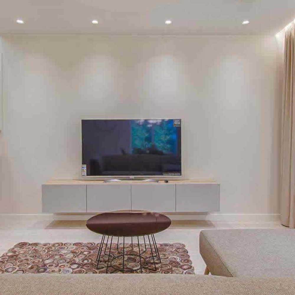 <span class="uk-h4">A modern living area with a beige sectional sofa, a flat-screen TV, a wooden staircase, and large windows, offering a bright and open design.</span>